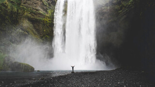 A huge waterfall in the background and a small figure standing at the bottom, raising their arms.